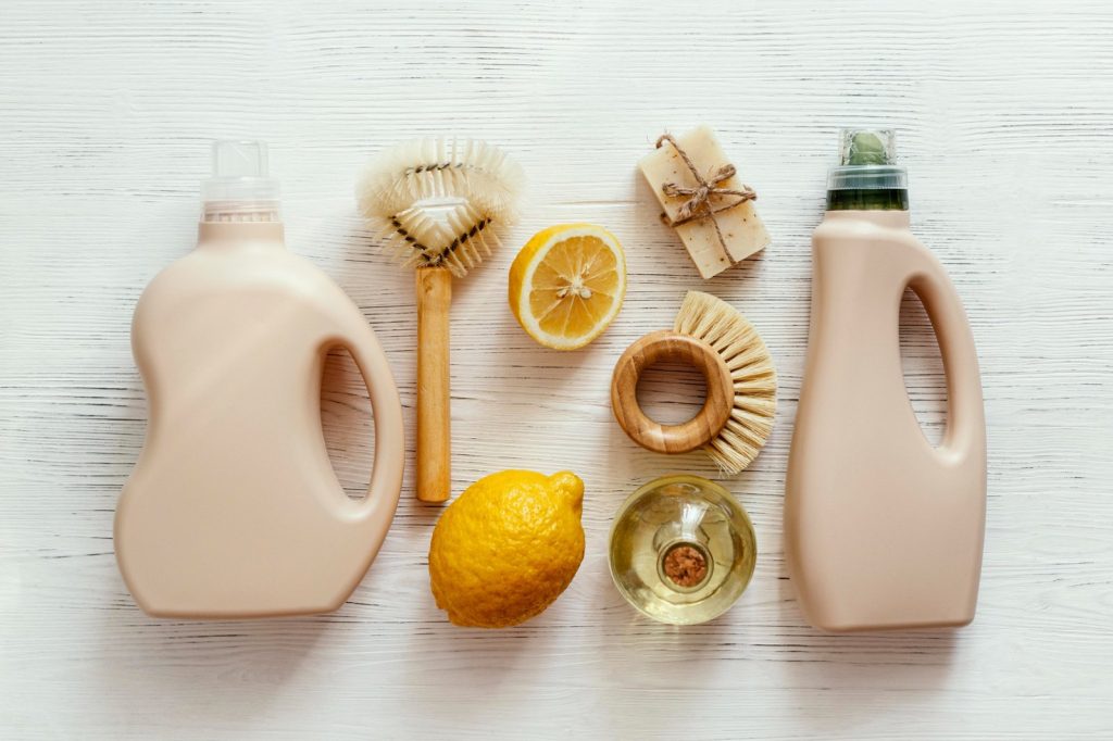 Eco-friendly cleaning products including lemon, vinegar, brushes, and detergent on a white background