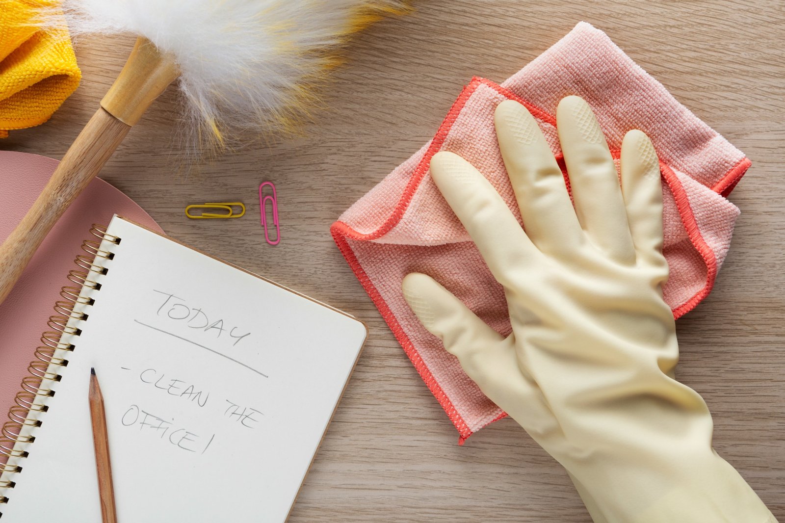 Rubber glove cleaning a desk near a notebook with a cleaning checklist